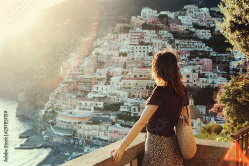 Young woman admiring panoramic view of Positano at sunset, Amalfi coast, Italy.Girl tourist stands with his back against the background of houses in Positano, a popular tourist destination in Italy