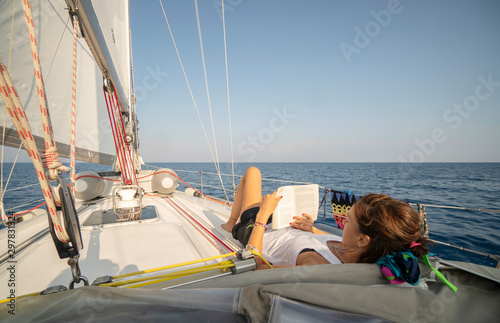 Young beautiful woman is relaxing and reading a book on a sailboat
