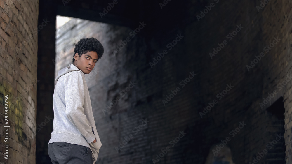 Obraz premium Black troubled teenager hanging around city building looking around, sadness