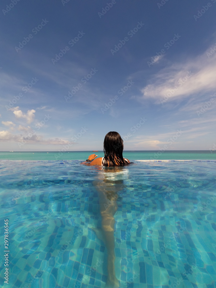 Rear view of a brunette woman in swimming pool looking at sea Rear view of a brunette woman in swimming pool looking at sea