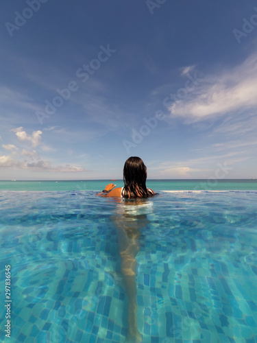 Rear view of a brunette woman in swimming pool looking at sea