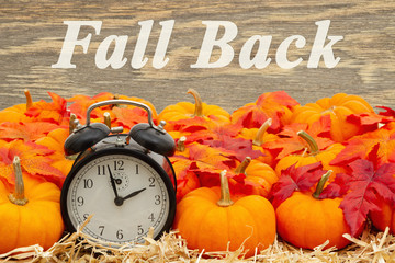 Fall Back time change message with a retro alarm clock with pumpkins and fall leaves