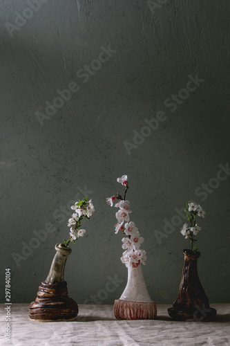 Spring blossom cherry and pear branches flowers in craft ceramic vases standing on grey linen table cloth. Spring interior. Copy space.