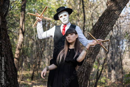 A masked puppeteer controlling and manipulating a girl. Girl portrays puppet. The concept of manipulation and control.. Halloween. photo