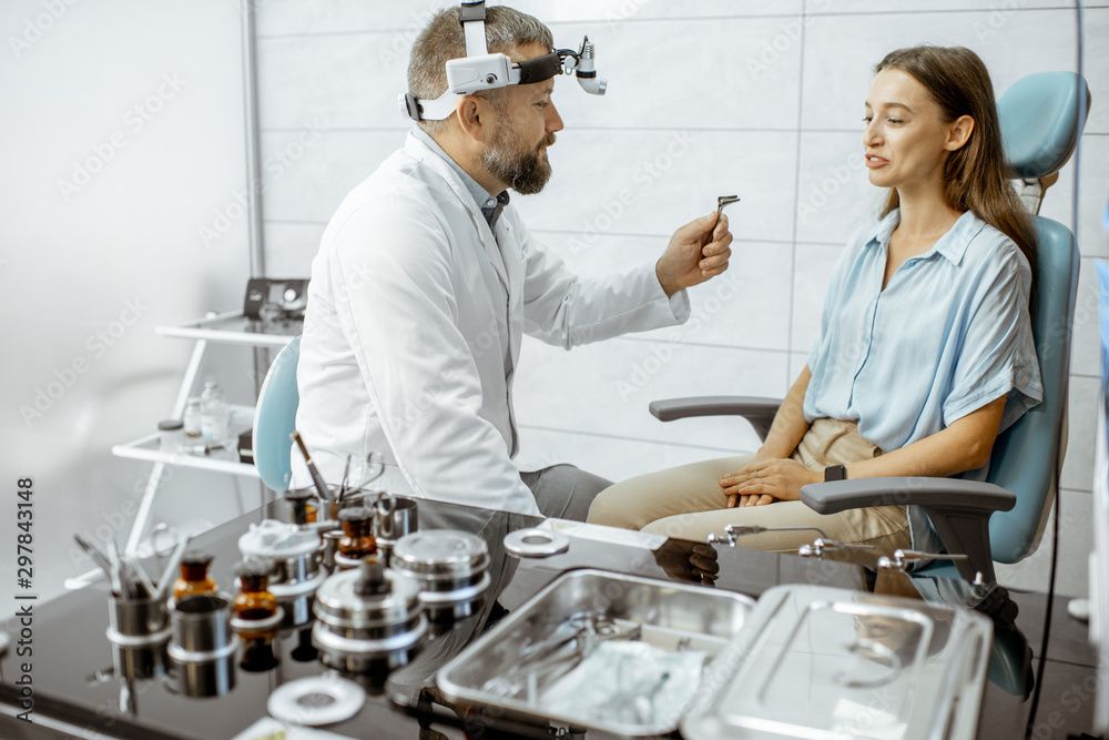 Fototapeta premium Senior otolaryngologist preparing for the medical examination procedure for a woman patient in the medical office with ENT workstation