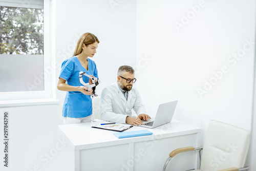 Senior otolaryngologist and female assistant having a medical meeting  working with laptop at the bright medical office interior