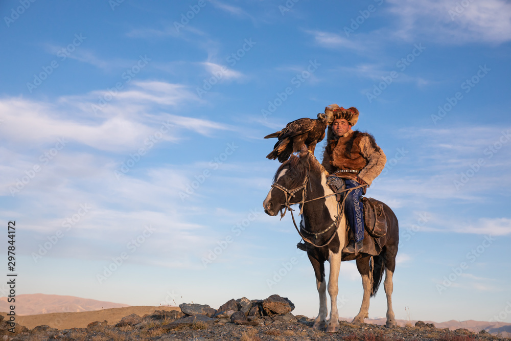 Naklejka premium Portrait of a traditional kazakh eagle hunter with his colorful horse and majestic golden eagle on a sunny day. Ulgii, Western Mongolia.