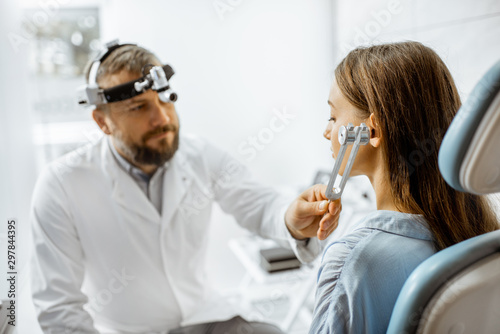 Senior otolaryngologist examining ears with ENT tuning fork for a young patient in the medical office. Hearing test with tuning fork concept photo