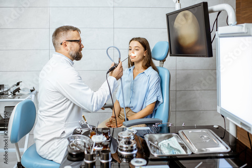 Schilderij op canvas Senior otolaryngologist making endoscopic examination of a nose for a young pati