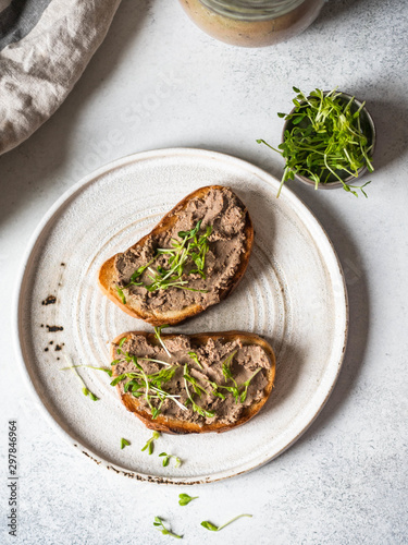Two toasts chicken rillettes (pate) on white bread with sprouts on white plate on a light background . Top view