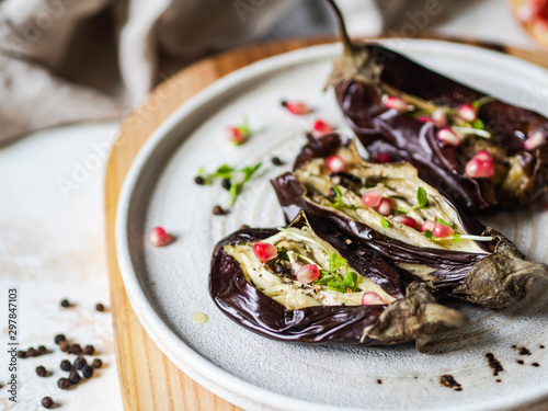 Baked eggplants slices with spices, sprouts, pomegranate and olive oil on a white ceramic plate on gray background.