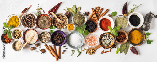 Various dry spices in small bowls and raw herbs flat lay on white background. Top view,