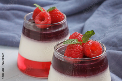 Berry jelly with raspberries in a glass cup on light blue background. Blue textile on the table.