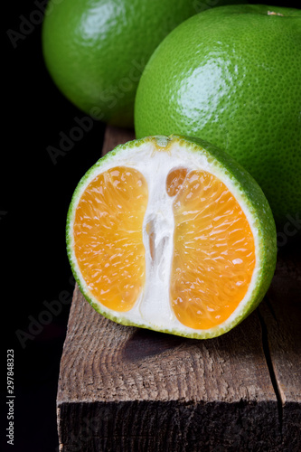 Green mandarins cut in halves and segments and whole sweetie on a wooden table