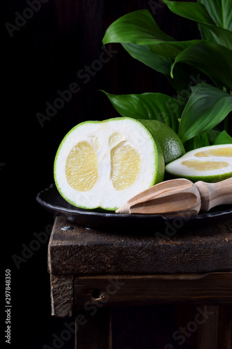 Sweetie cut into halves on a stone plate on the edge of the wooden table against black background