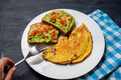 Healthy breakfast with omelette and guacamole toast on dark background