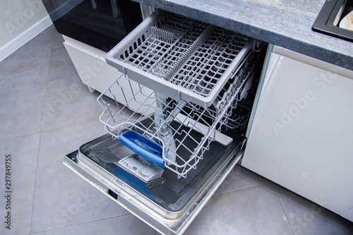 open modern dishwasher in the kitchen; built-in appliances in furniture.