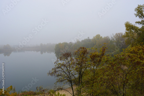 Beautiful landscape  autumnal nature with white dense fog over Career Lake  Dnipro city  Ukraine. Tall trees and large shrubs with yellow leaves around a clean and beautiful lake.