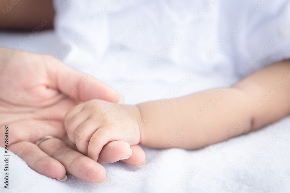 Close up baby's hand holding her mother's hand on the white cloth mattress in the lawn
