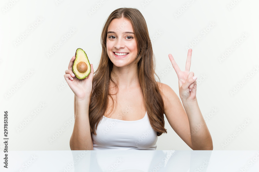 Young caucasian woman holding an avocado showing number two with fingers. Young caucasian woman holding an avocado showing number two with fingers.
