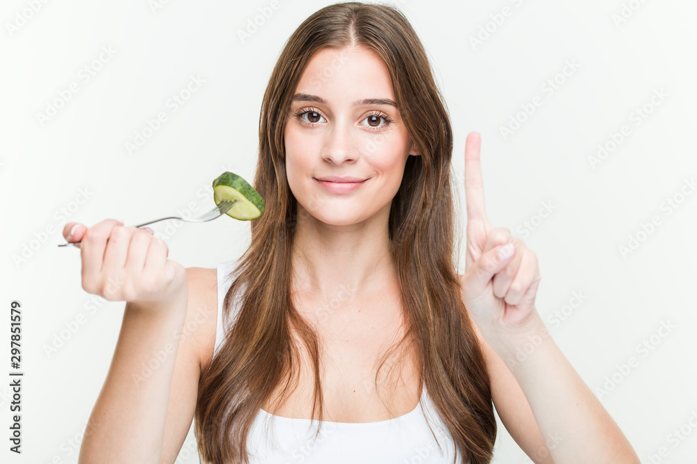 Young caucasian woman eating cucumber showing number one with finger. Young caucasian woman eating cucumber showing number one with finger.