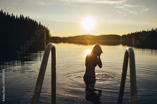 Fototapeta Naklejka Na Ścianę i Meble -  Young woman swimming in the lake at sunset after sauna in Finland
