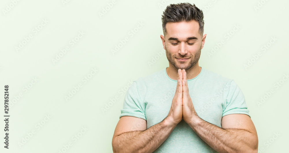Young handsome man against a green background holding hands in pray near mouth, feels confident. Young handsome man against a green background holding hands in pray near mouth, feels confident.