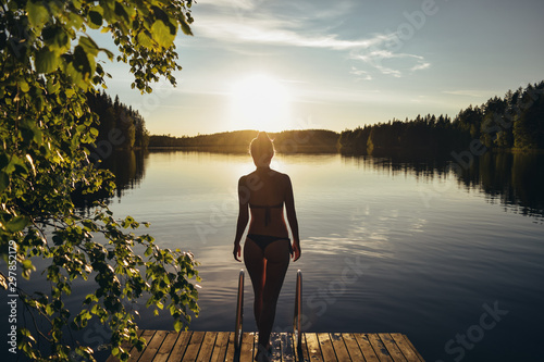 Young woman going into the lake from pier at sunset after sauna in Finland