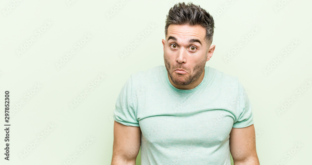 Young handsome man against a green background shrugs shoulders and open eyes confused. Young handsome man against a green background shrugs shoulders and open eyes confused.