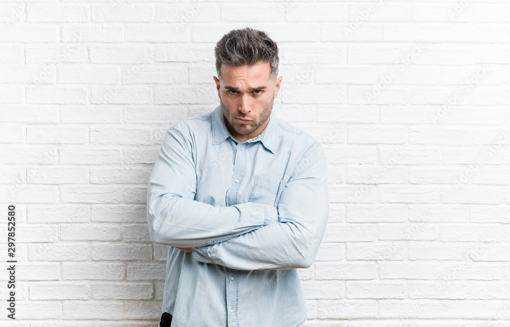 Young handsome man against a bricks wall frowning face in displeasure, keeps arms folded. Young handsome man against a bricks wall frowning face in displeasure, keeps arms folded.