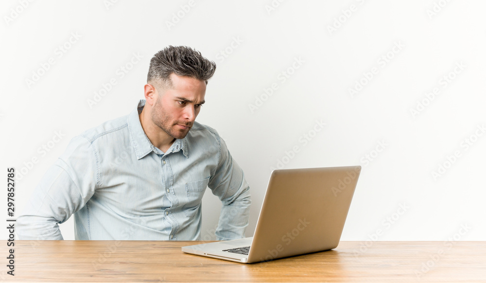 Young handsome man working with his laptop confident keeping hands on hips. Young handsome man working with his laptop confident keeping hands on hips.