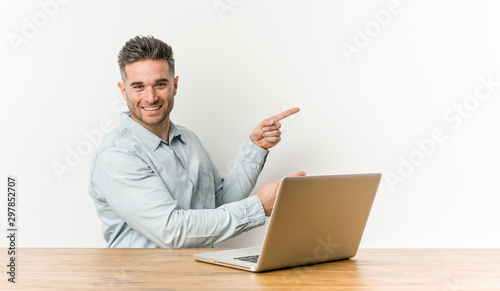 Young handsome man working with his laptop excited pointing with forefingers away.
