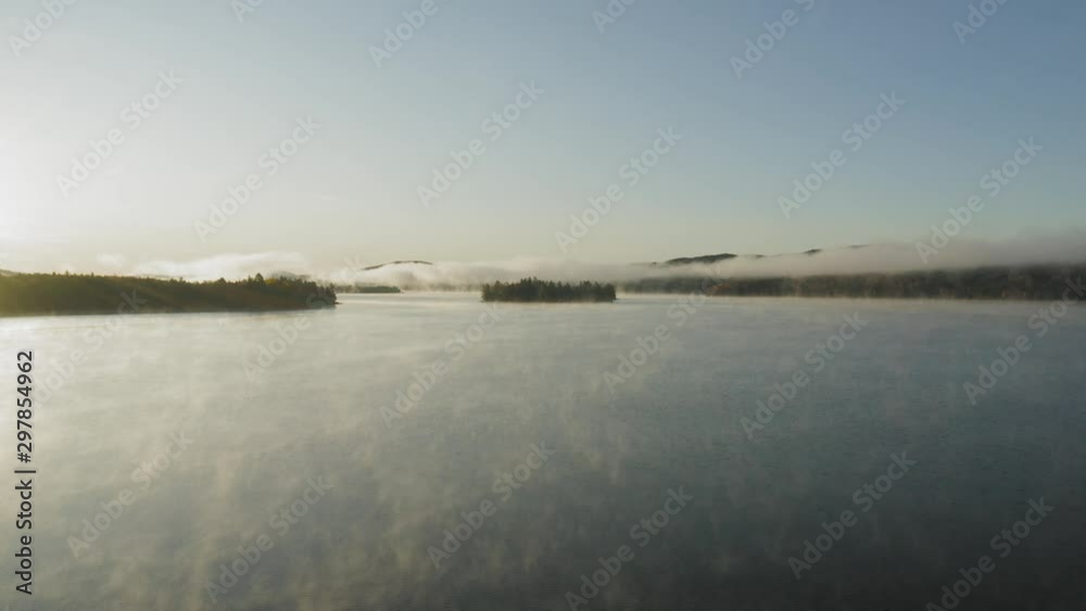 Flying low and fast above a mist covered lake at sunrise with a lens flare AERIAL Flying low and fast above a mist covered lake at sunrise with a lens flare AERIAL