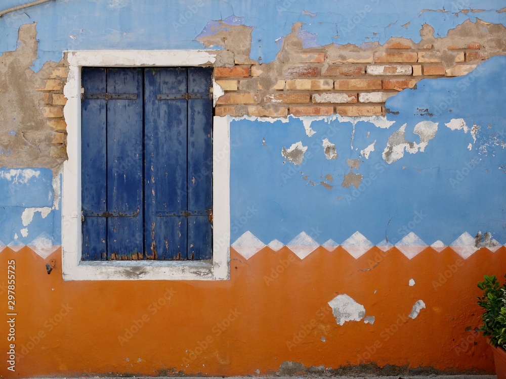 A wall with paint peeling and window with blue shutters