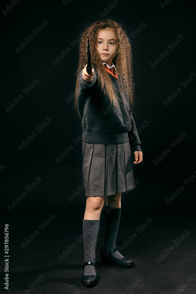 Portrait of a little witch girl with long brown hair dressed in dark clothes, holding magic wand in her hand, posing on black studio background. Portrait of a little witch girl with long brown hair dressed in dark clothes, holding magic wand in her hand, posing on black studio background.