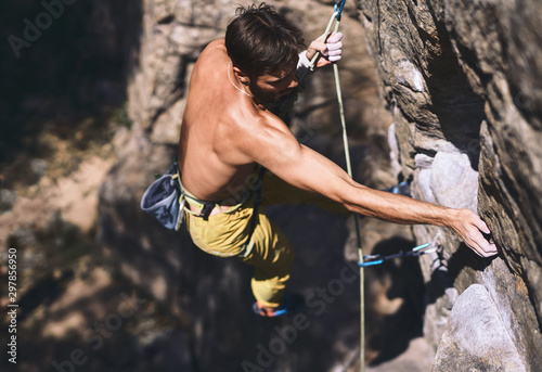 Close up portrait of strong muscular man rockclimber climbing on tough sport route, resting and chalking hands.