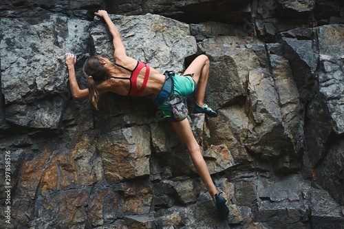 young slim muscular woman rockclimber climbing on tough sport route, climber makes a hard move.