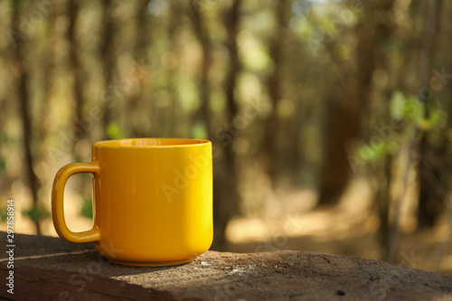 Yellow cup on board. Beautiful forest, space for text