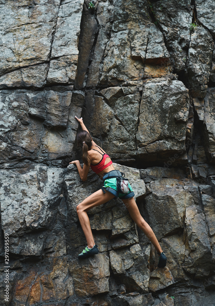 young slim muscular woman rockclimber climbing on tough sport route, climber makes a hard move.