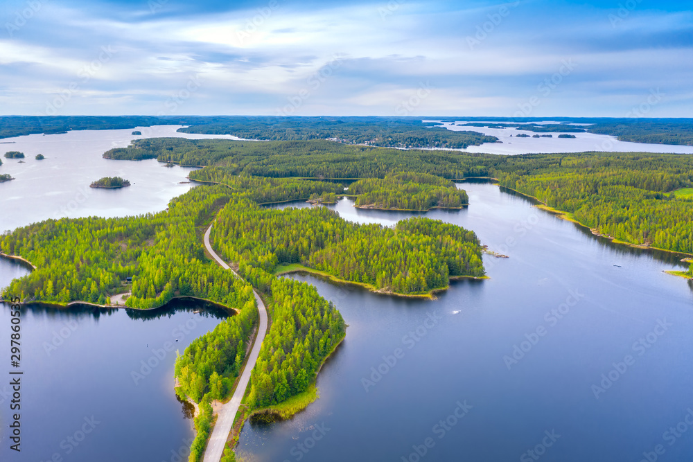 Aerial view of road between green summer forest and blue lake in Finland. Saimaa lake, Puumala.