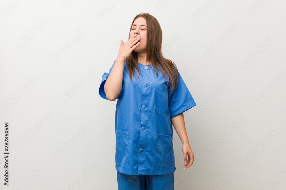Young nurse woman against a white wall yawning showing a tired gesture covering mouth with hand. Young nurse woman against a white wall yawning showing a tired gesture covering mouth with hand.