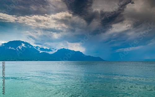 Landscape of Alps mountains,lake Geneva,cloudy dark sky with rain in the distance. Shot taken from the shore of the lake in Montreux, Switzerland. 