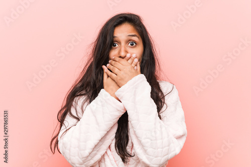 Young indian woman wearing pajama shocked covering mouth with hands.