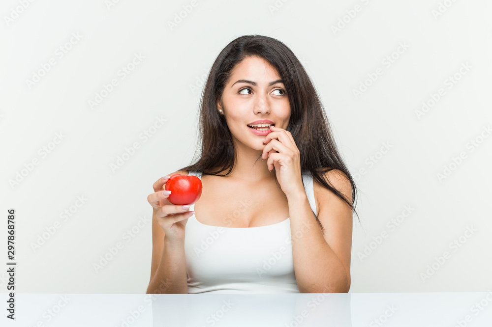 Young hispanic woman holding a tomato relaxed thinking about something looking at a copy space. Young hispanic woman holding a tomato relaxed thinking about something looking at a copy space.