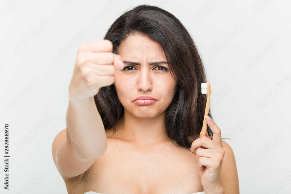 Young hispanic woman holding a toothbrush showing fist to camera, aggressive facial expression. Young hispanic woman holding a toothbrush showing fist to camera, aggressive facial expression.