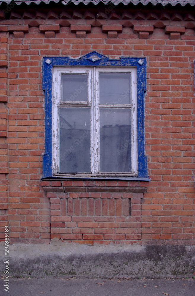 Fototapeta premium Antique wooden white window with blue carved frame and red brick wall without modern elements in the afternoon