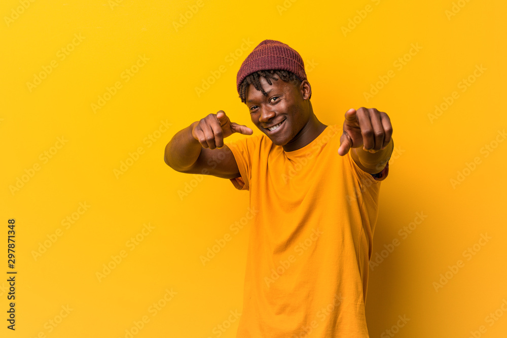 © Asier - Young black man wearing rastas over yellow background cheerful smiles pointing to front. © Asier - Young black man wearing rastas over yellow background cheerful smiles pointing to front.