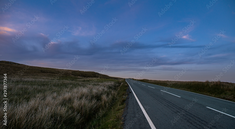 Fototapeta premium Road through green landscapes in the sunset