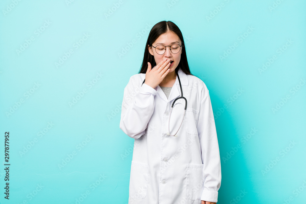 Young chinese doctor woman yawning showing a tired gesture covering mouth with hand. Young chinese doctor woman yawning showing a tired gesture covering mouth with hand.