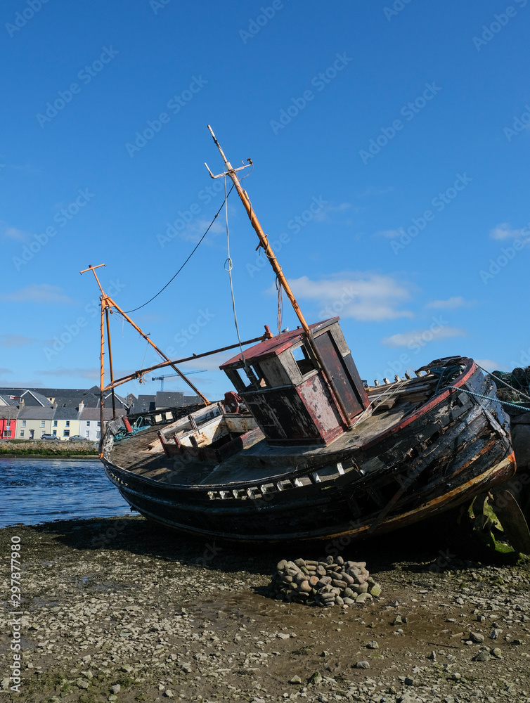Old wooden shipwreck at the edge of the Corrib River as it flows into Galway Bay, Ireland showing the decayed wood, and houses in the background, taken on a sunny summer day. Old wooden shipwreck at the edge of the Corrib River as it flows into Galway Bay, Ireland showing the decayed wood, and houses in the background, taken on a sunny summer day.